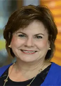 A woman with brown hair and blue jacket smiling.