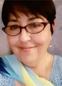 A woman with glasses and short hair wearing a blue shirt.