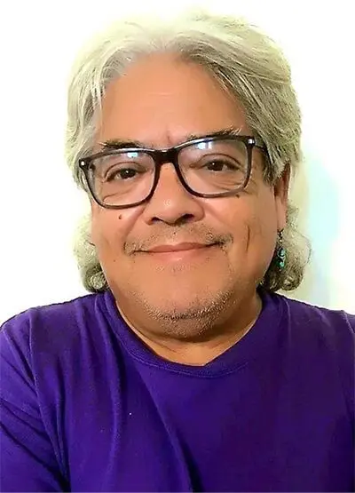 A man with glasses and long hair wearing a purple shirt.