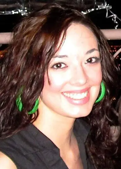 A woman with long brown hair wearing green earrings.